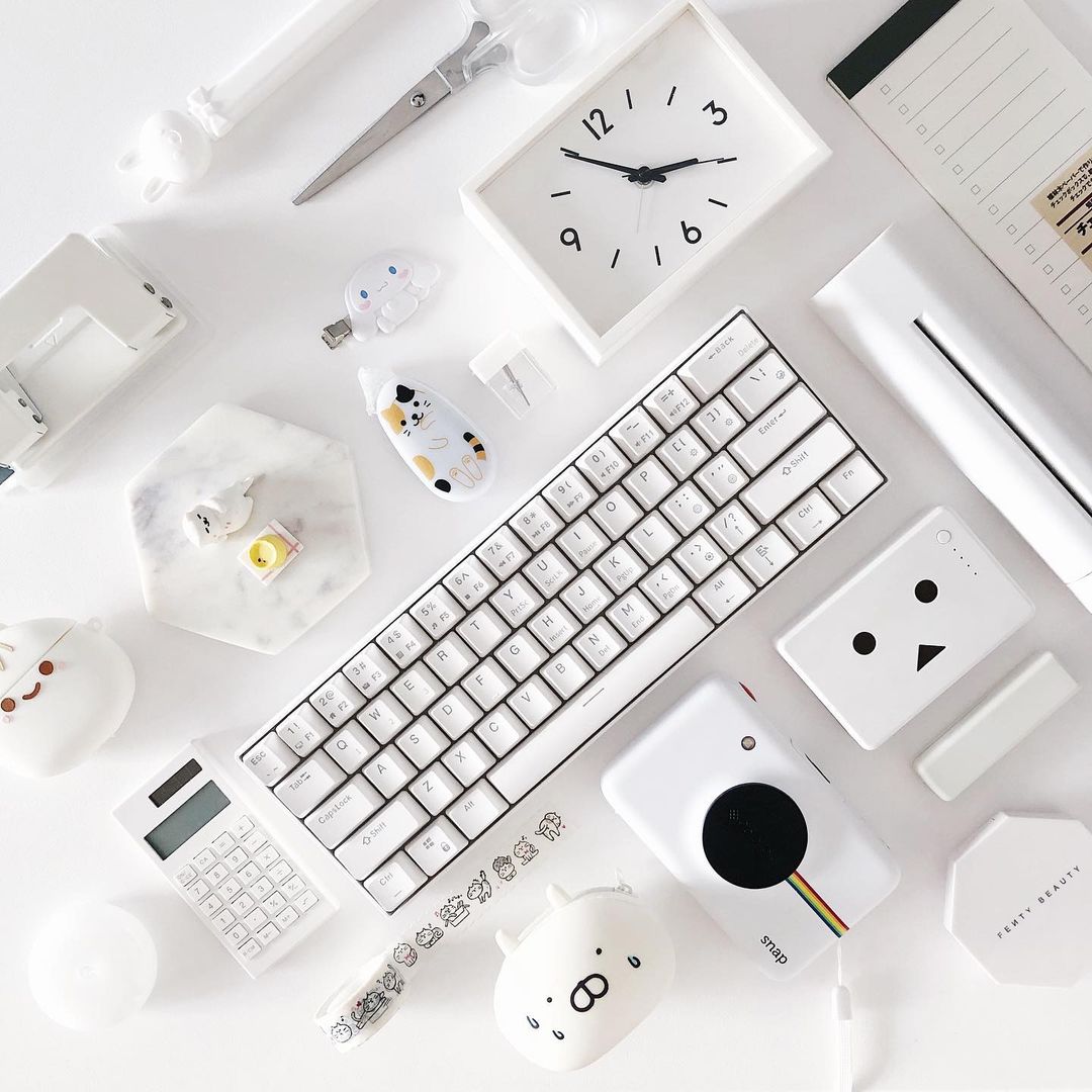 Flat lay of a desk featuring a Royal Kludge RK61 keyboard, a clock, and various office supplies arranged neatly